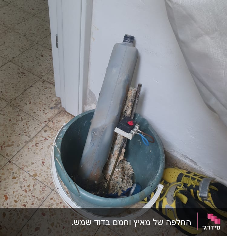 דלי עם כלים וחלקי צנרת ליד נעליים